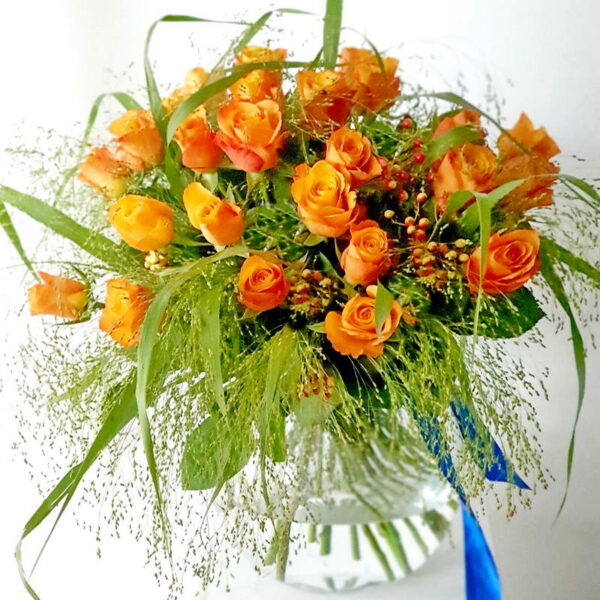 Bukiet 'Coral Charisma' z pomarańczowych róż i akcentów zielonej trawy, wykończony niebieską wstążką