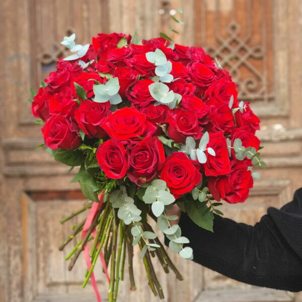 Bukiet 'Miłość' składający się z głęboko czerwonych róż i srebrzystych liści eukaliptusa na tle drewnianych drzwi.